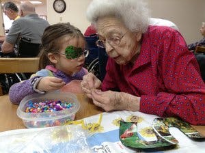 Child with eye patch and older person doing crafts with beads