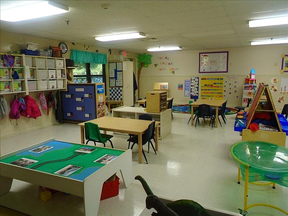 An empty classroom with tables, chairs, shelving, and play areas