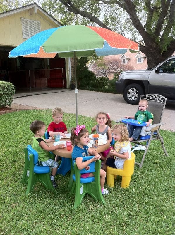 Children sitting at a small table with an umbrella outdoors