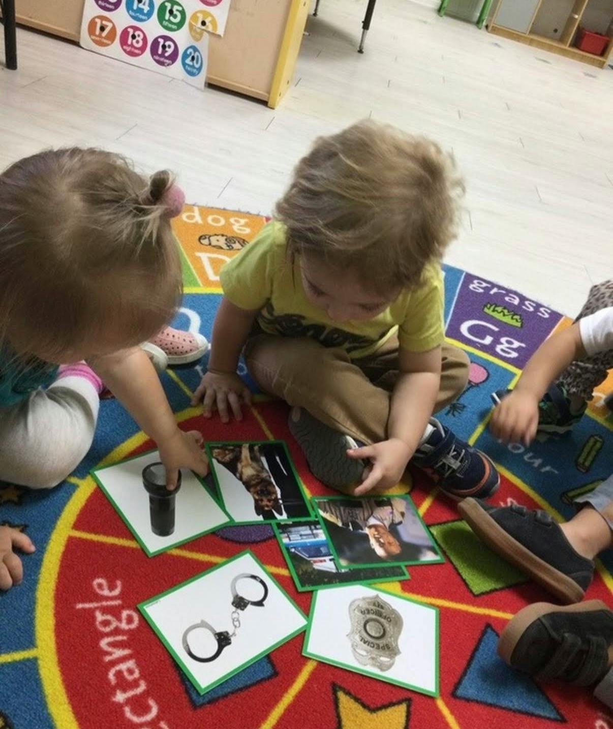 Children on a rug playing with cards showing a flashlight, handcuffs, and a badge