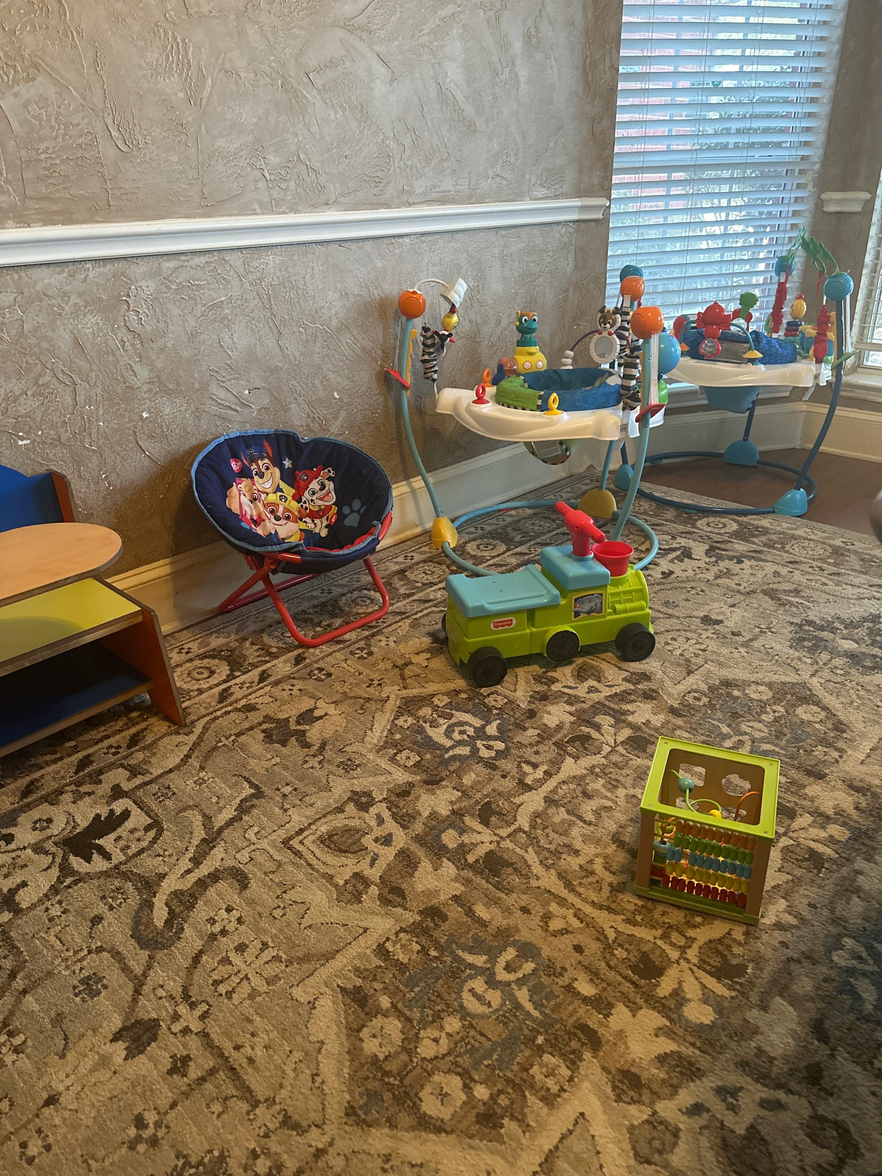 Baby play items including a bouncer, activity center, and other toys on a rug
