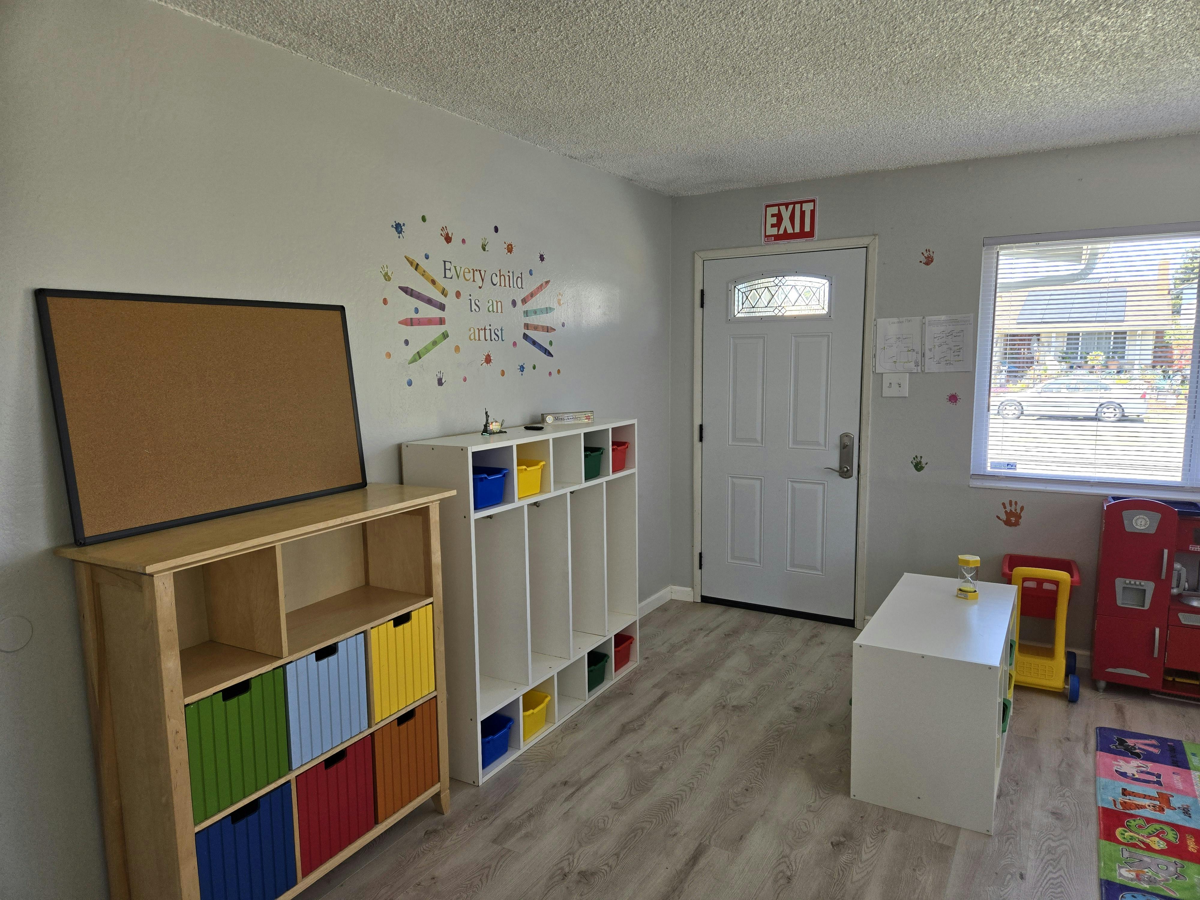 Room with storage shelves, a cork board, and a door with an exit sign