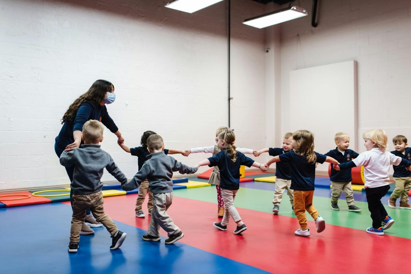 Person and children holding hands in a circle on a colorful mat