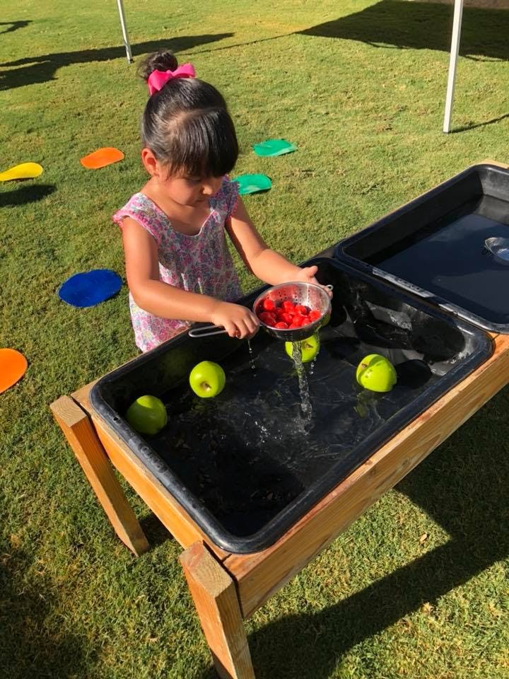 Child playing with water and berries in a sensory table