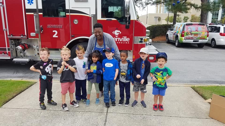 Adult and multiple children standing in front of a fire truck