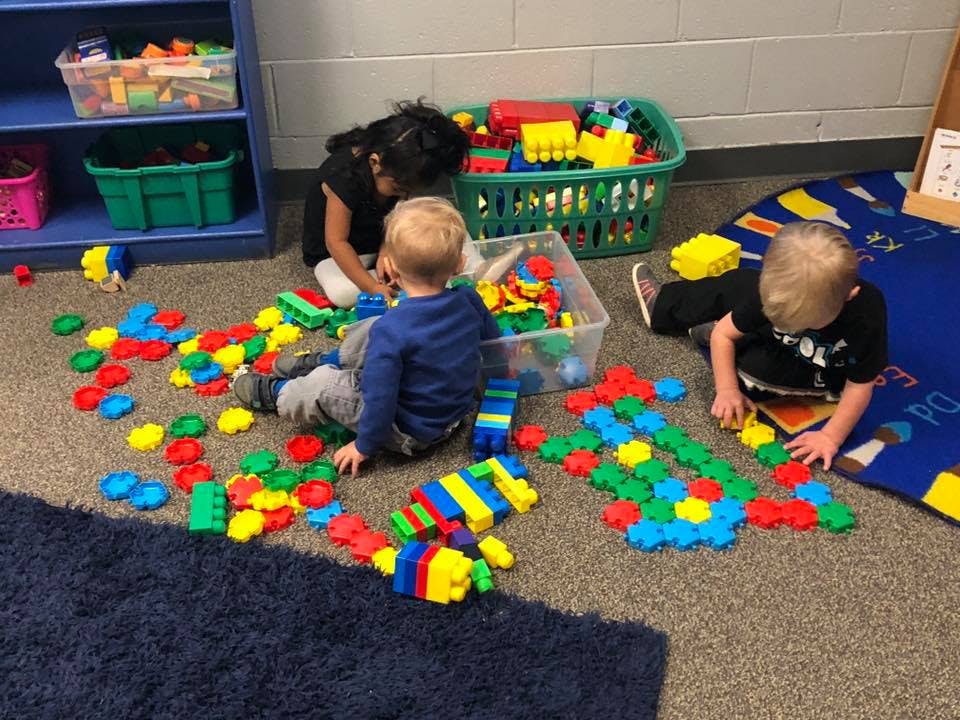 Three children playing with colorful building blocks on a carpeted floor