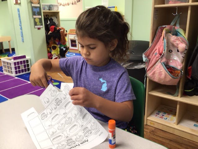 Child cutting paper at a table in a classroom