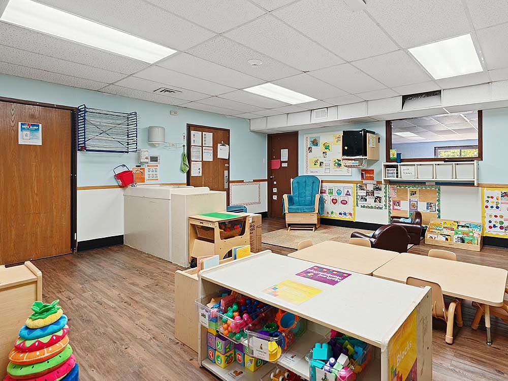Children's classroom with small tables and chairs, shelves of toys, and bulletin boards