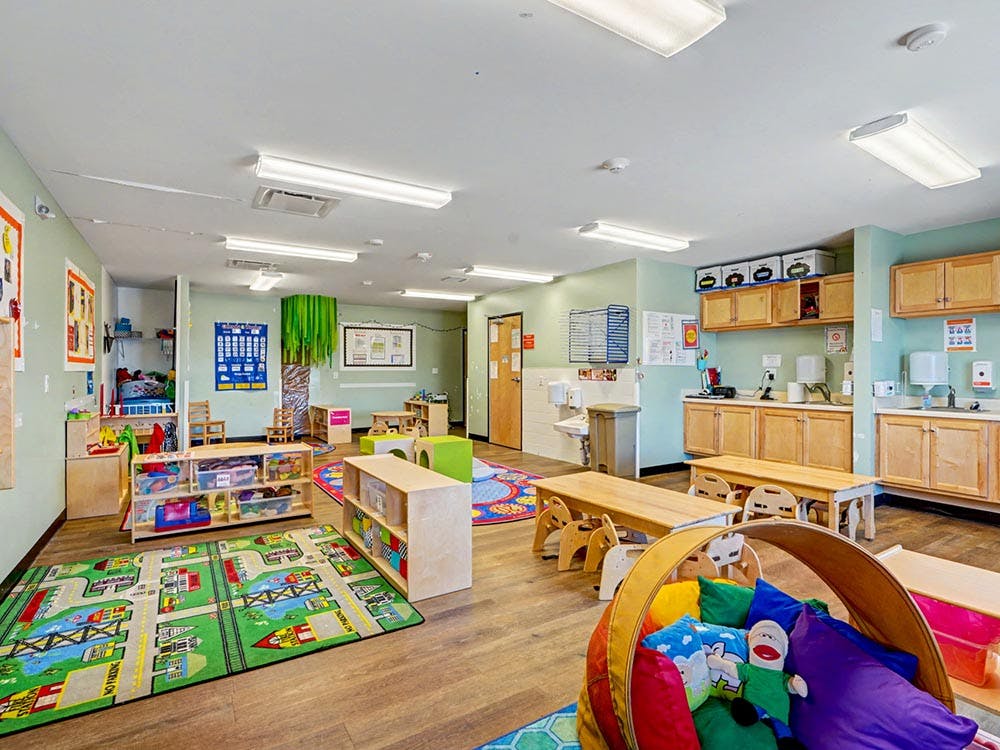 A colorful empty classroom with small wooden furniture and rugs
