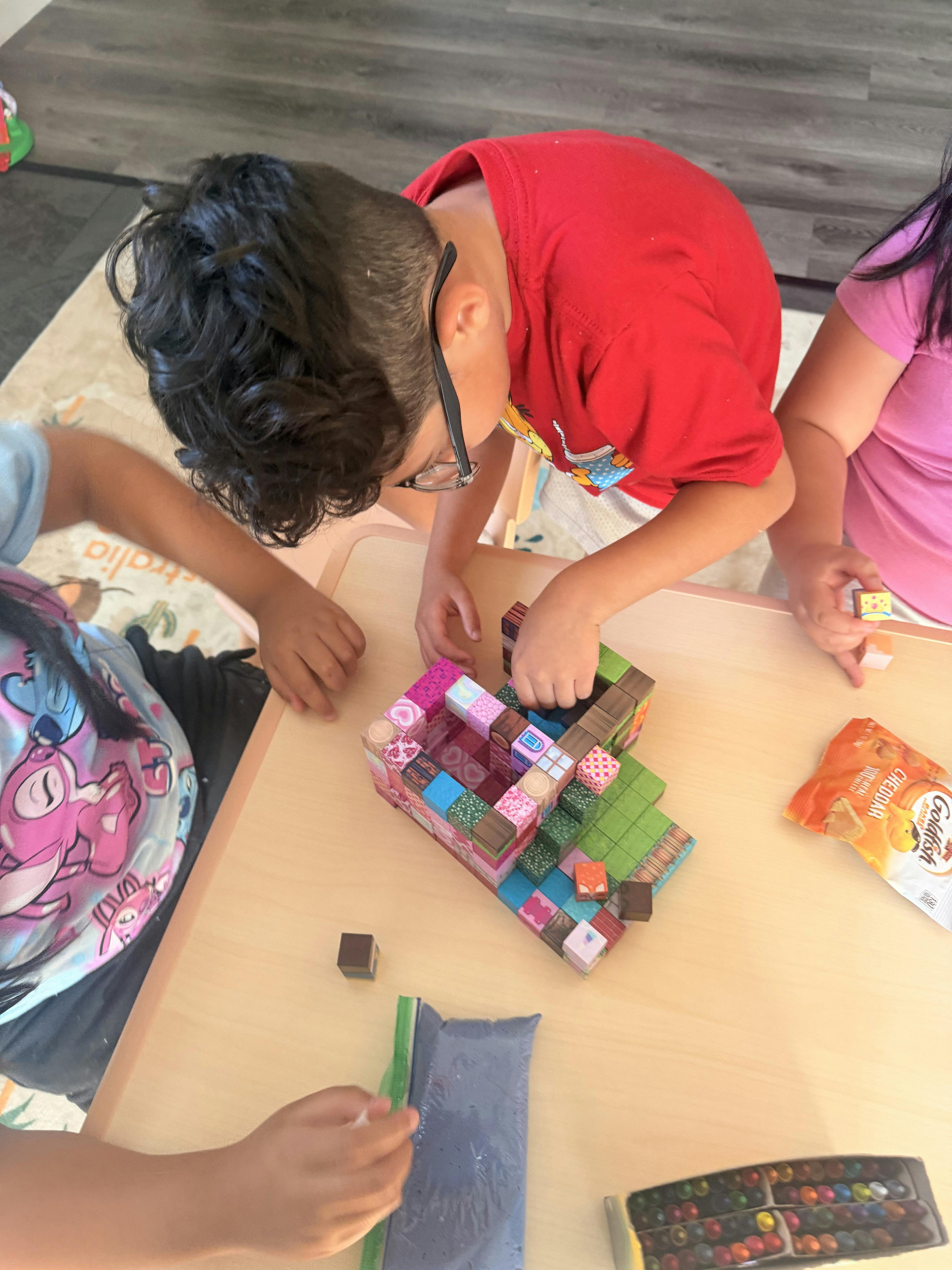 Children building a structure with patterned square blocks on a table