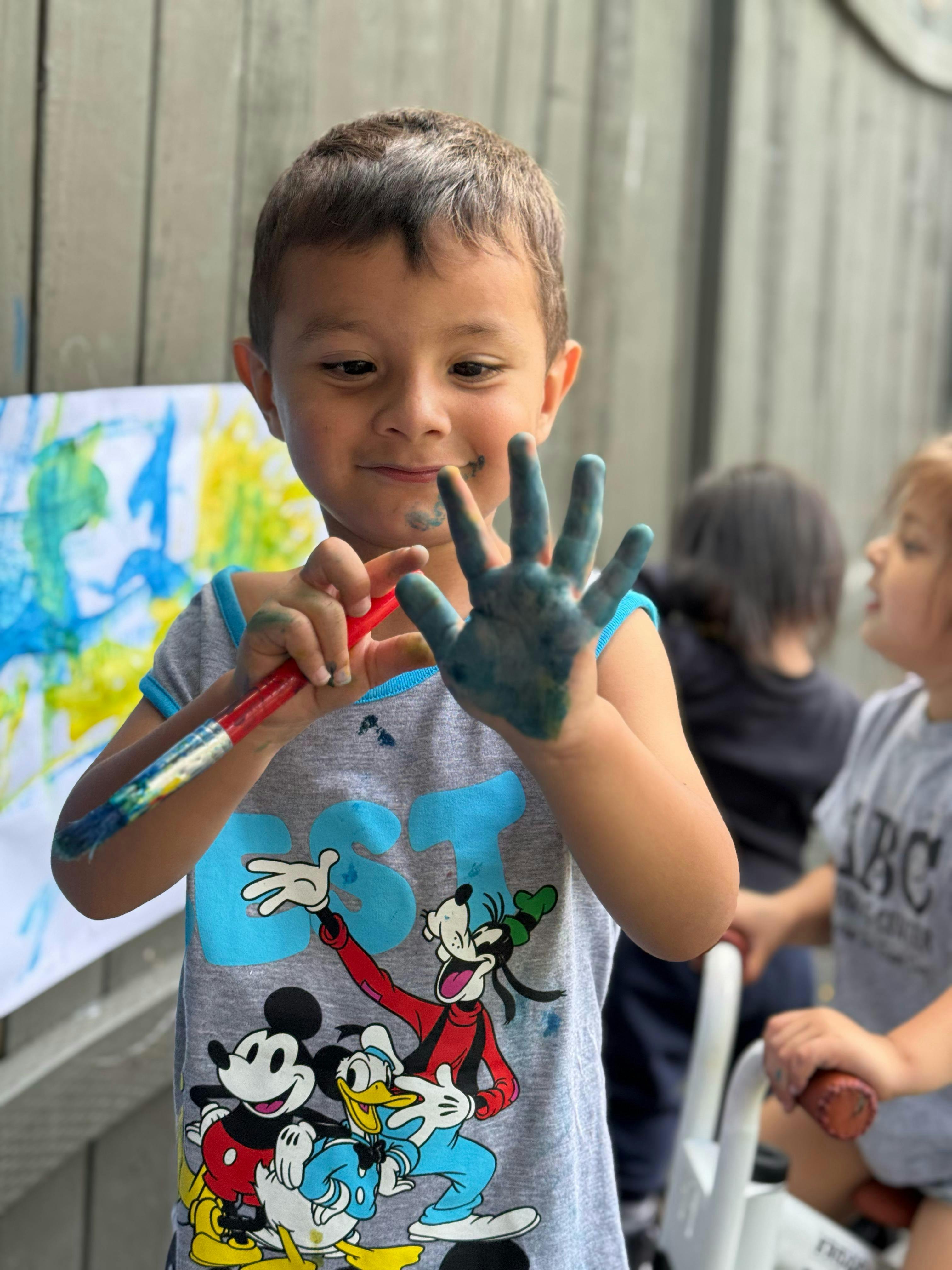 Child holding a paintbrush with blue paint on one hand