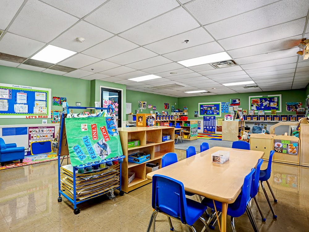 An empty early childhood classroom with tables, chairs, and shelves