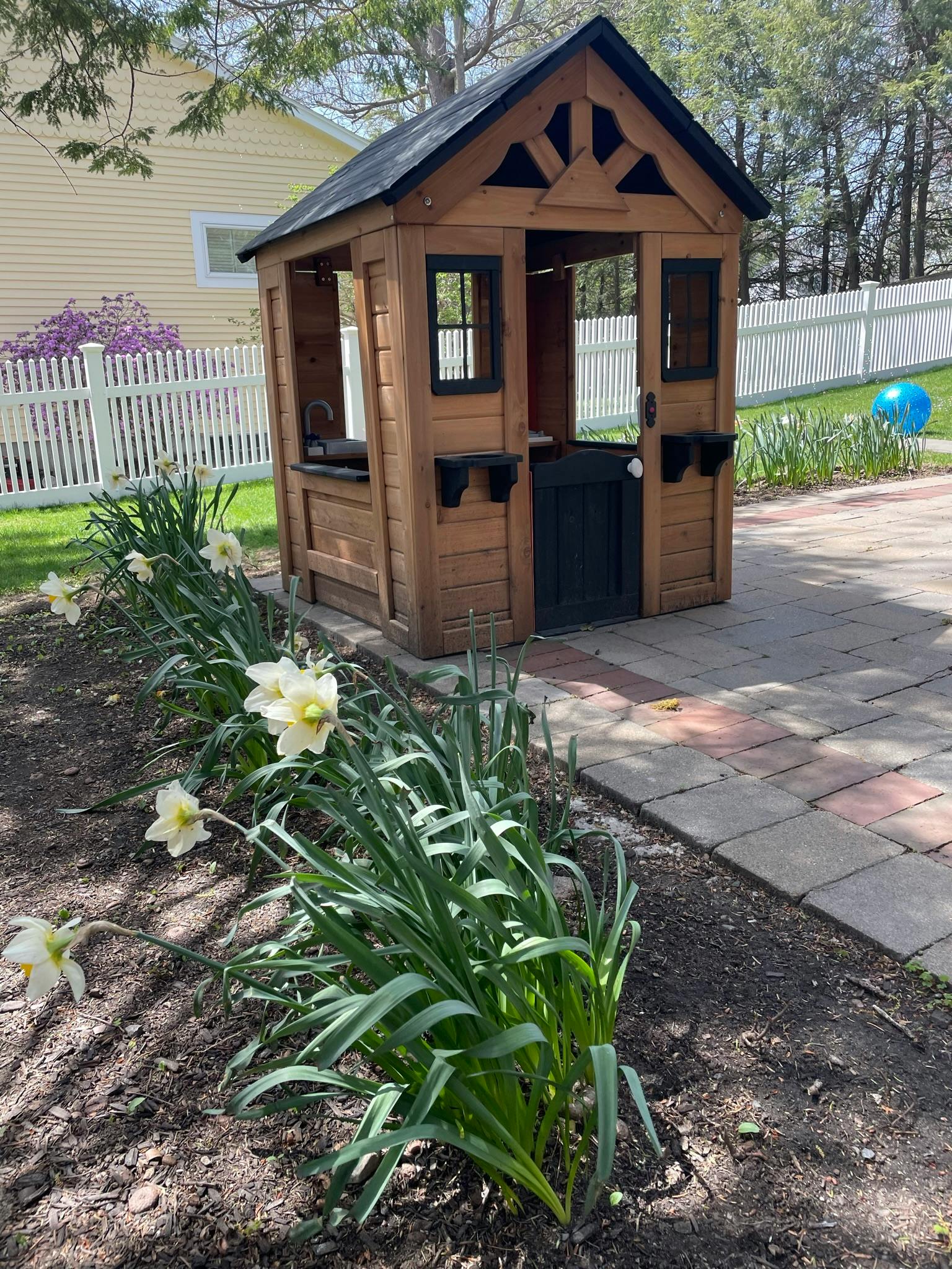 Wooden playhouse next to a flower bed with white daffodils