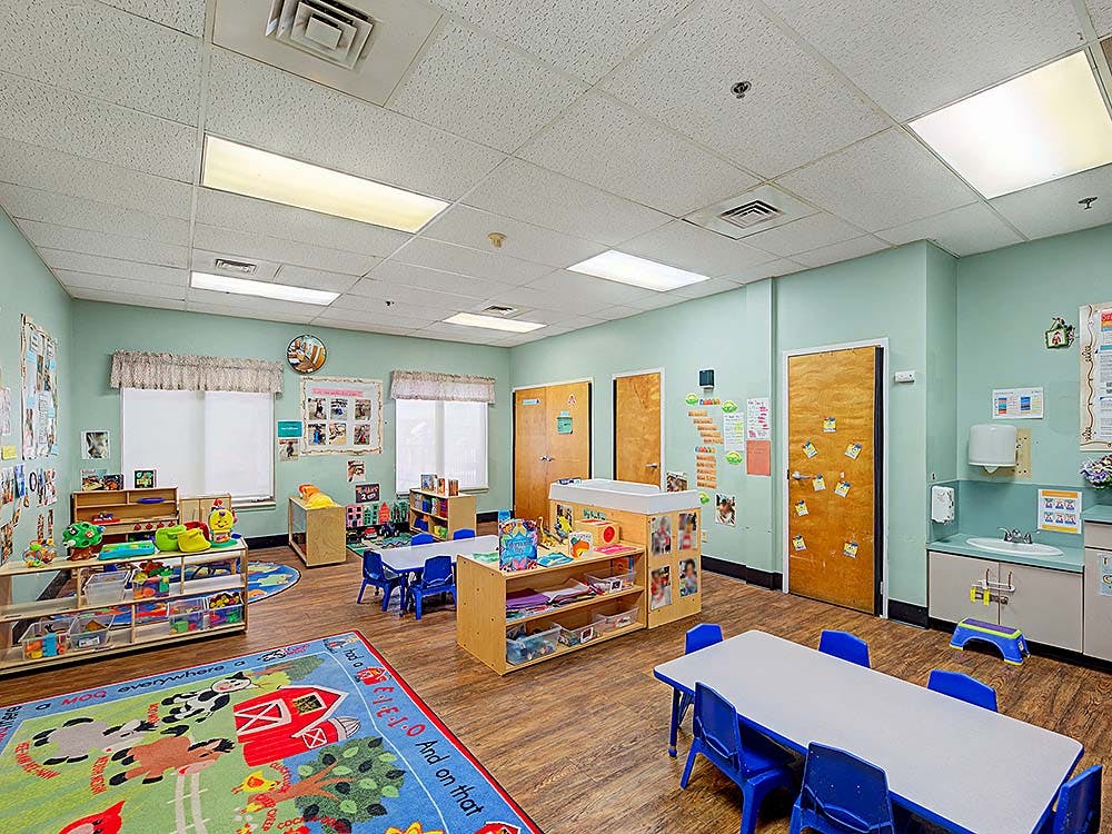 Empty colorful daycare classroom with tables, chairs, and play mats