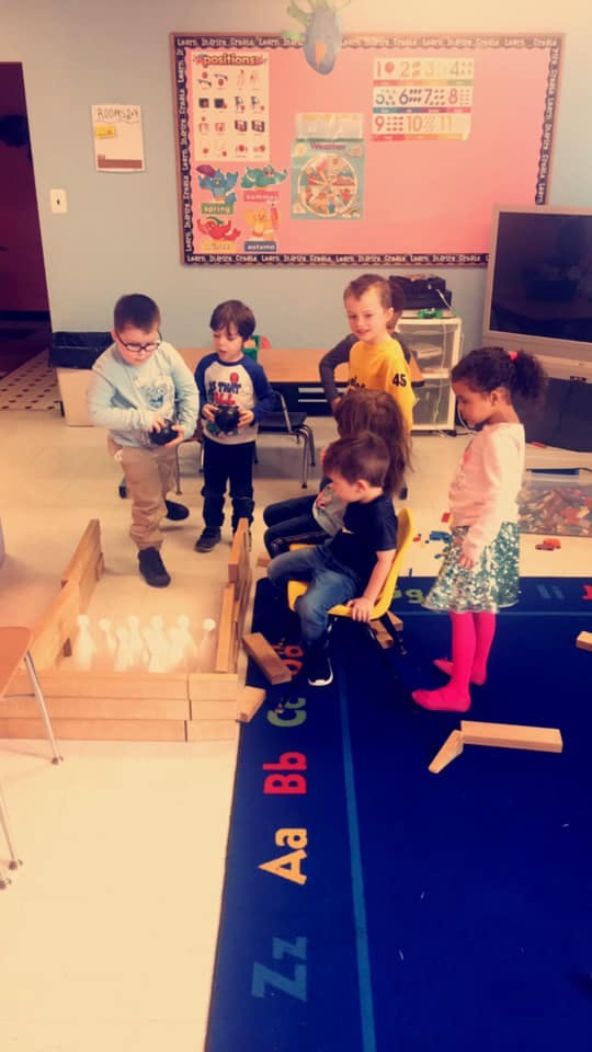 Children playing with a bowling set in a classroom