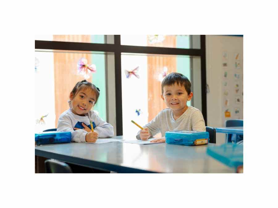 Two children writing at a table in a classroom