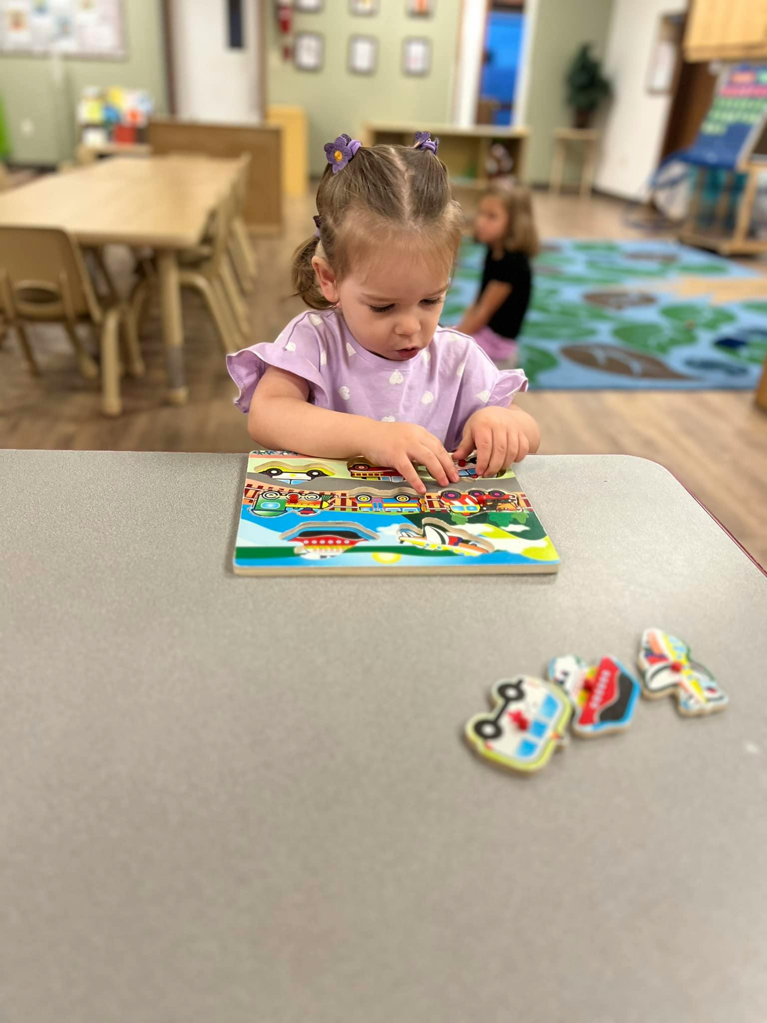 Child playing with a puzzle on a table in a classroom