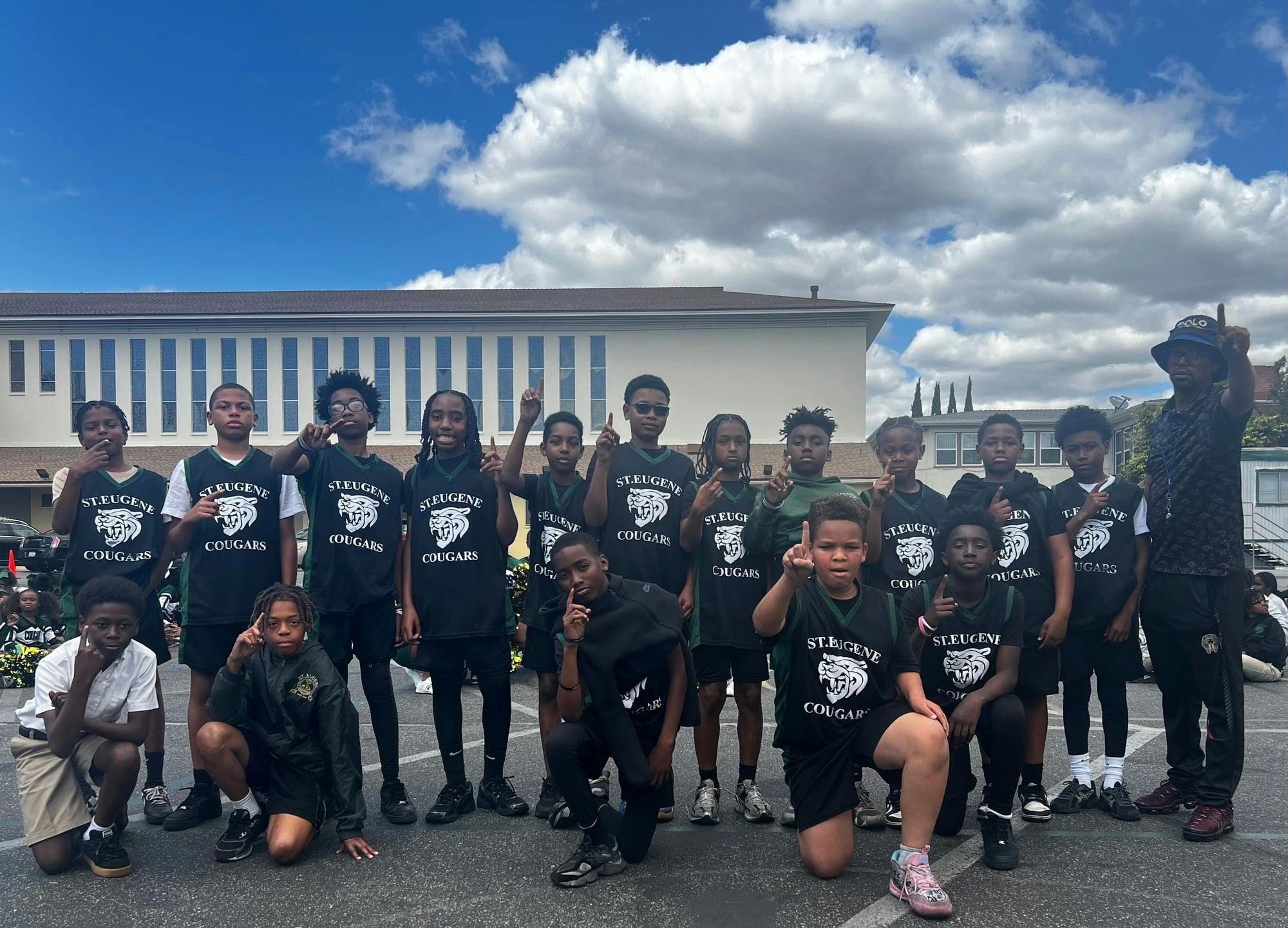Group of children and adults wearing St. Eugene Cougars shirts, some pointing to the sky
