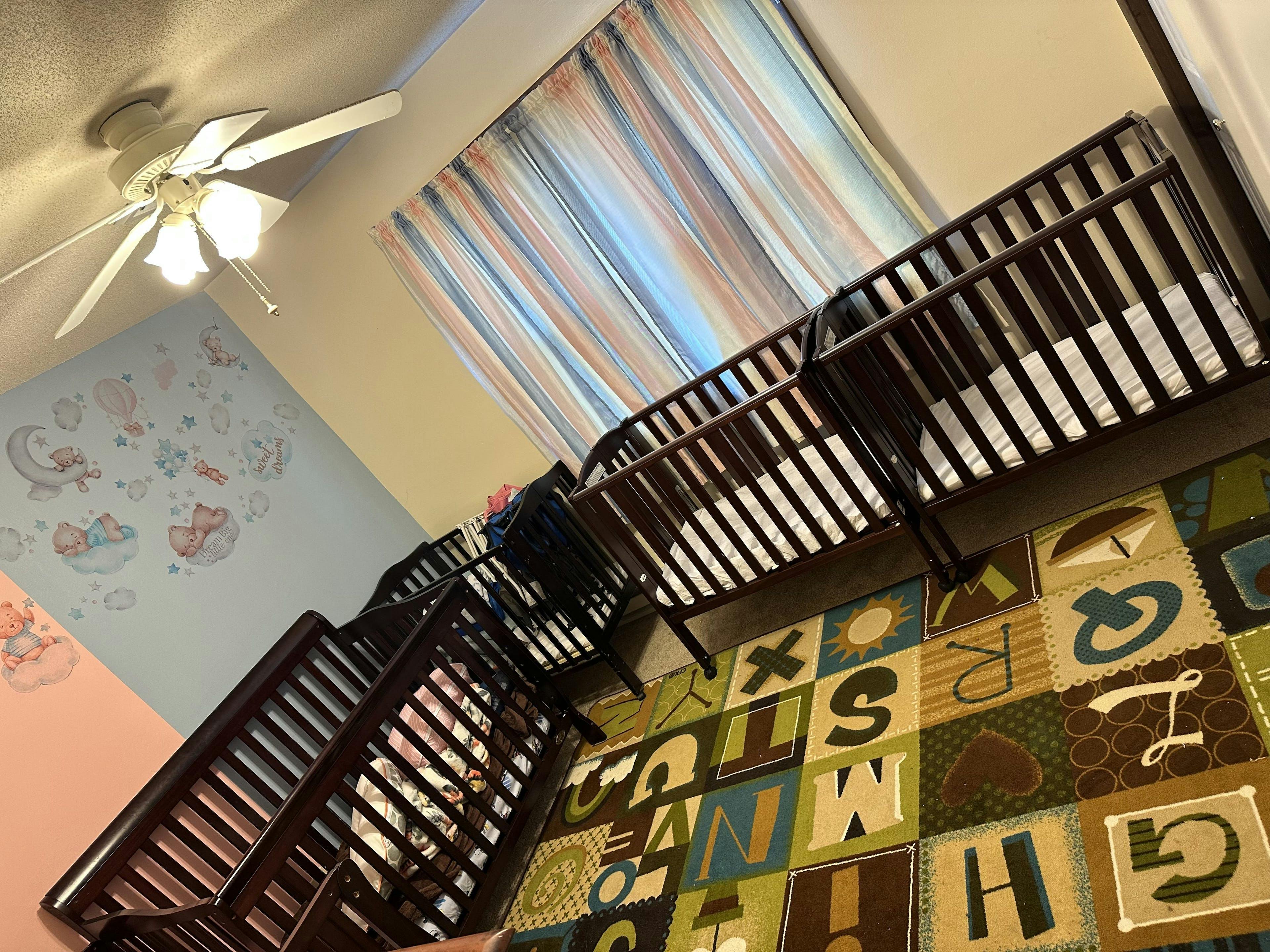 Two cribs in a room with an alphabet rug