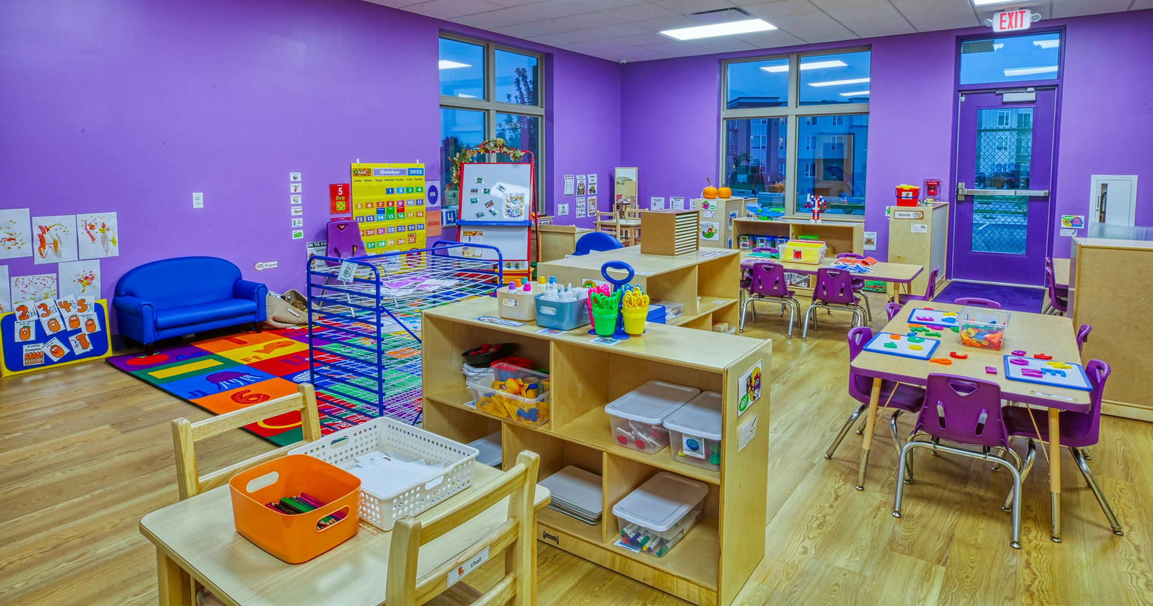 A colorful empty classroom with purple walls, small tables, and chairs