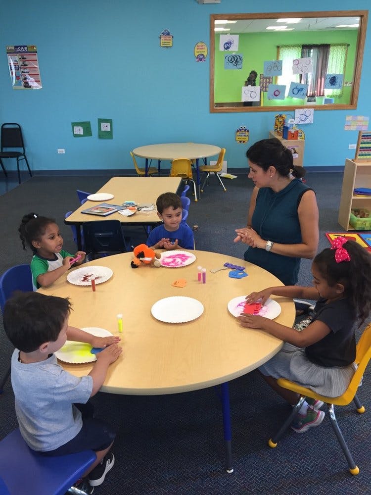 Adult and children doing crafts at a table in a classroom