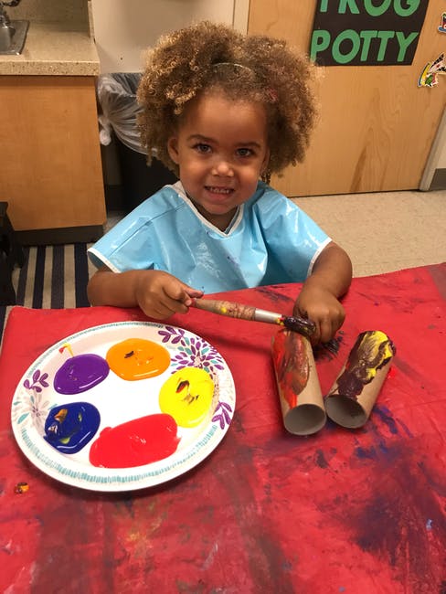 Child painting cardboard tubes with a brush and paint palette