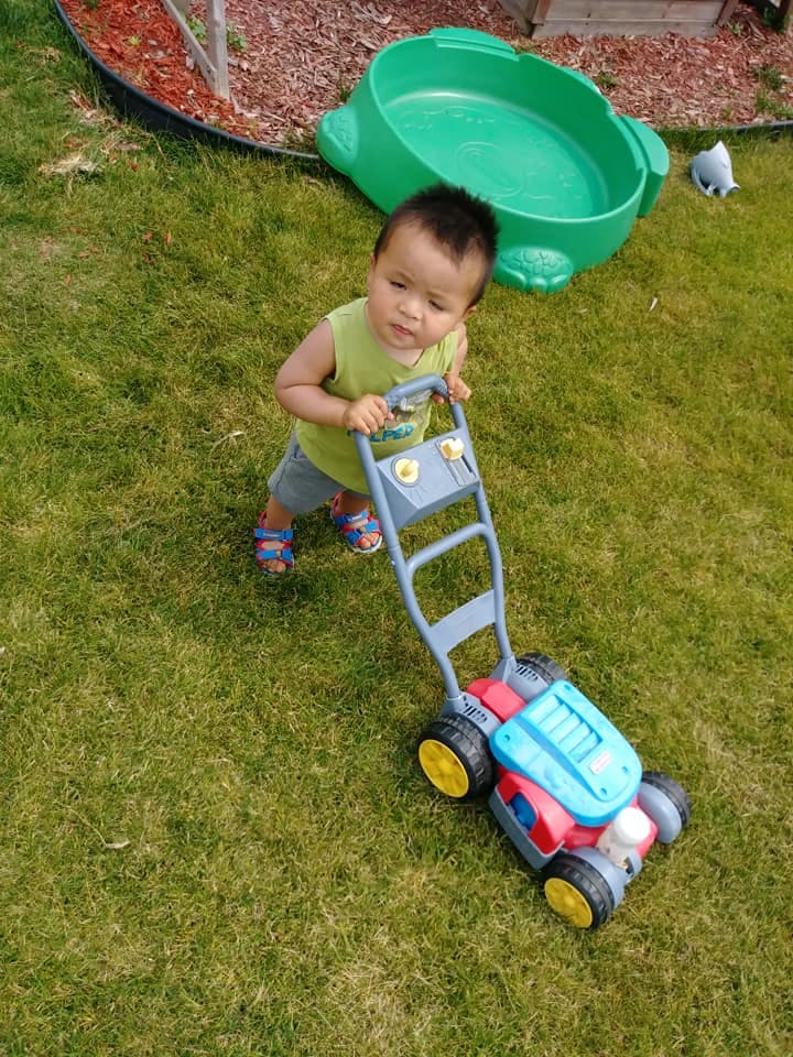Child pushing a toy lawnmower on grass