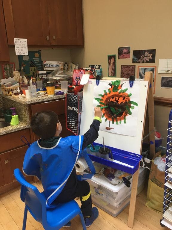 Child in a blue smock painting at an easel