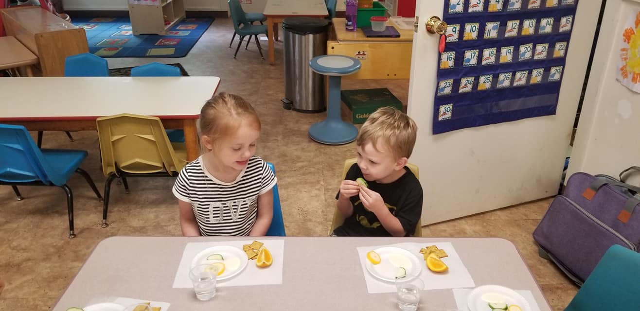 Two children eating at a table in a classroom