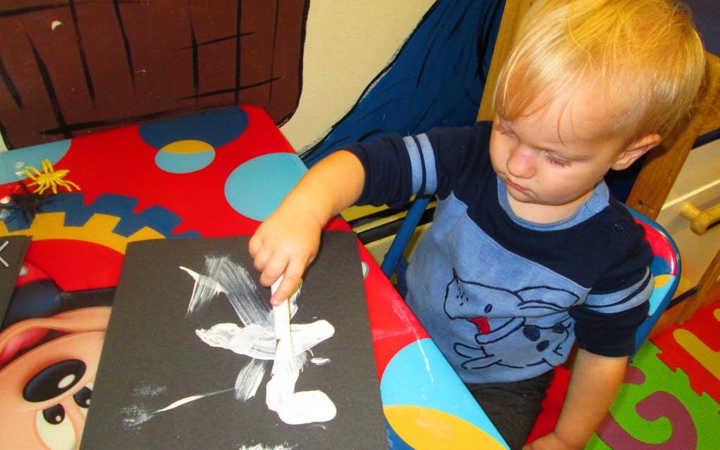 Child painting on a black surface with white paint