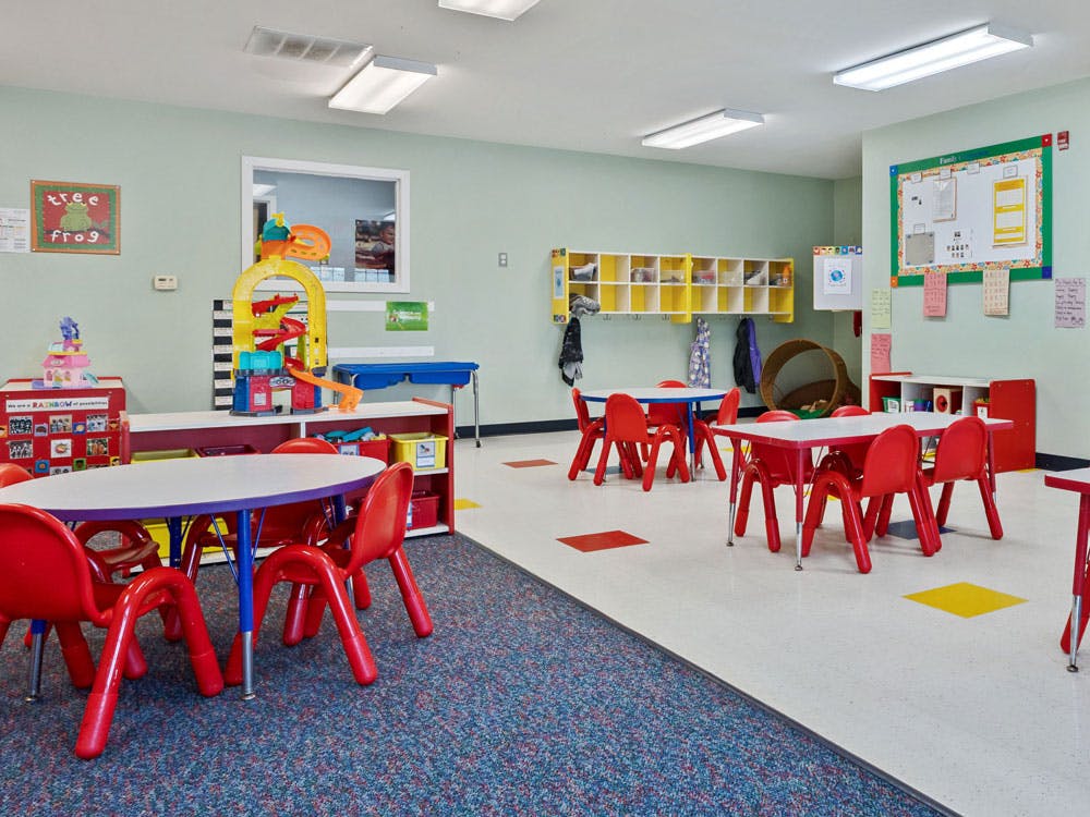 Empty classroom with small tables and chairs, shelves, and play equipment