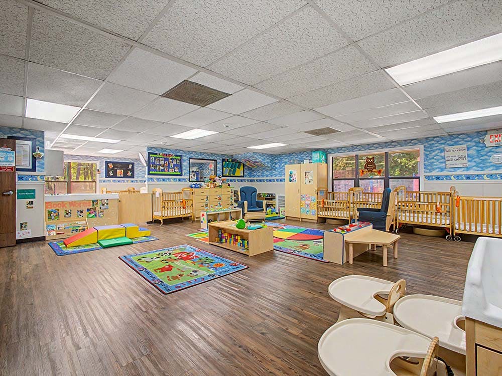 Empty infant classroom with cribs, play mats, and learning centers