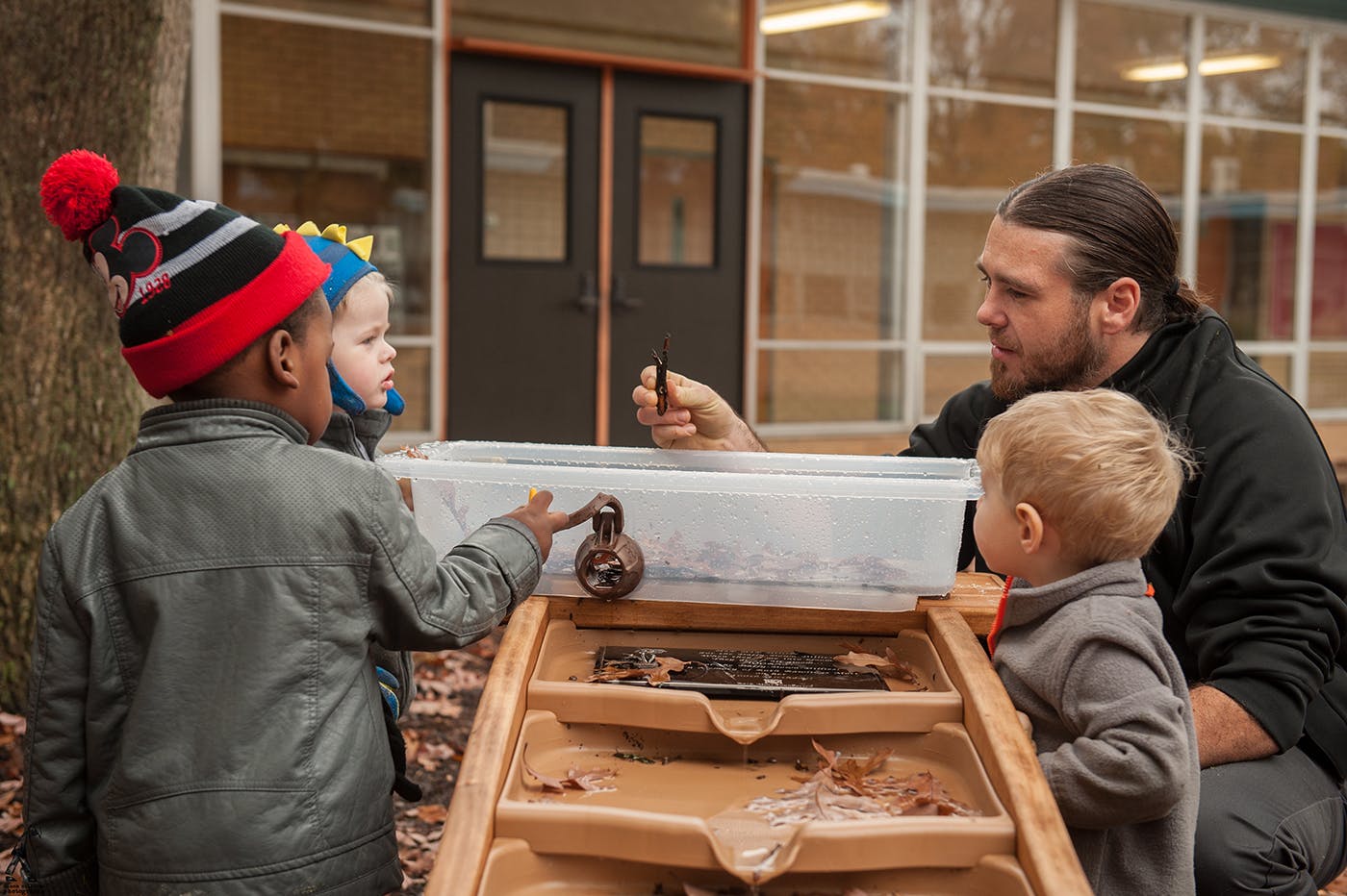 Adult and two children playing with water table outdoors