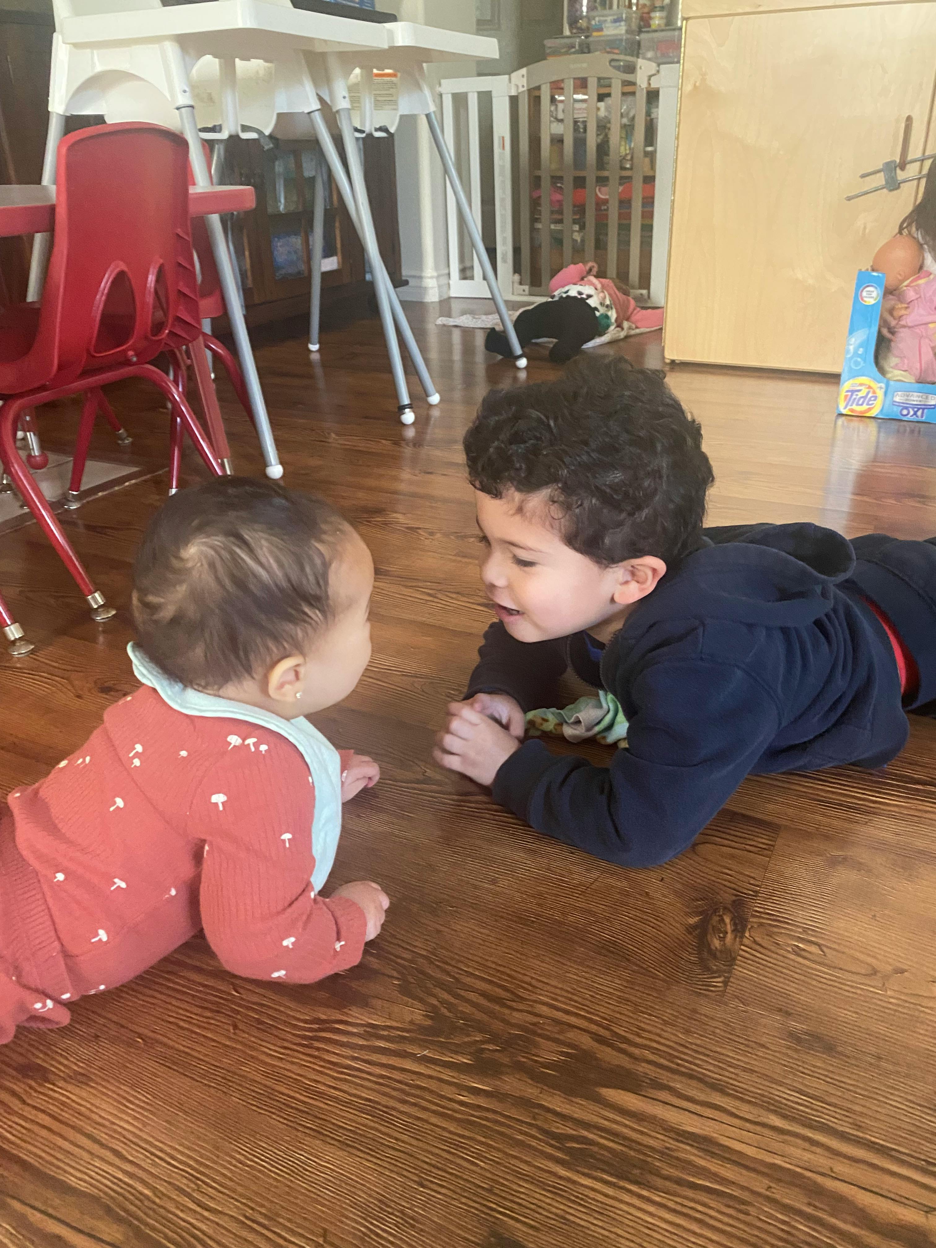 Child and baby lying on a wooden floor facing each other