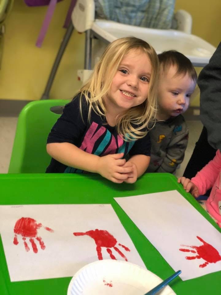 Child smiling at a table with handprint paintings