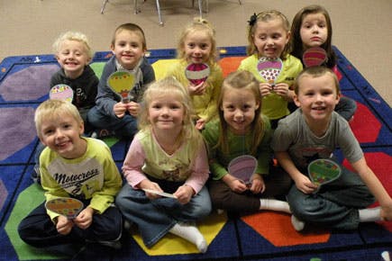 Group of children sitting on a colorful rug holding paper crafts