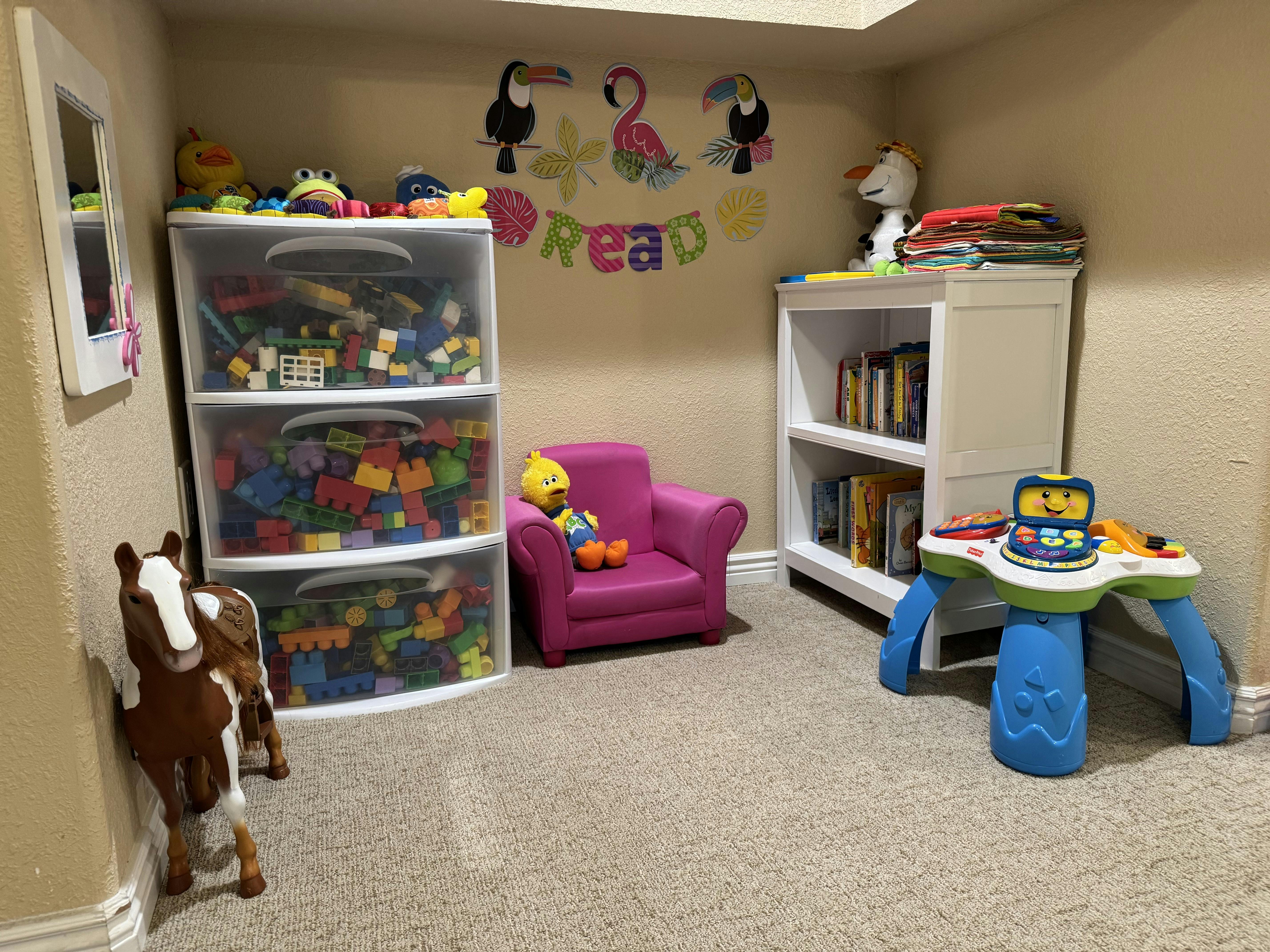 A playroom with toy storage, a small armchair, a bookshelf, a toy horse, and an activity table
