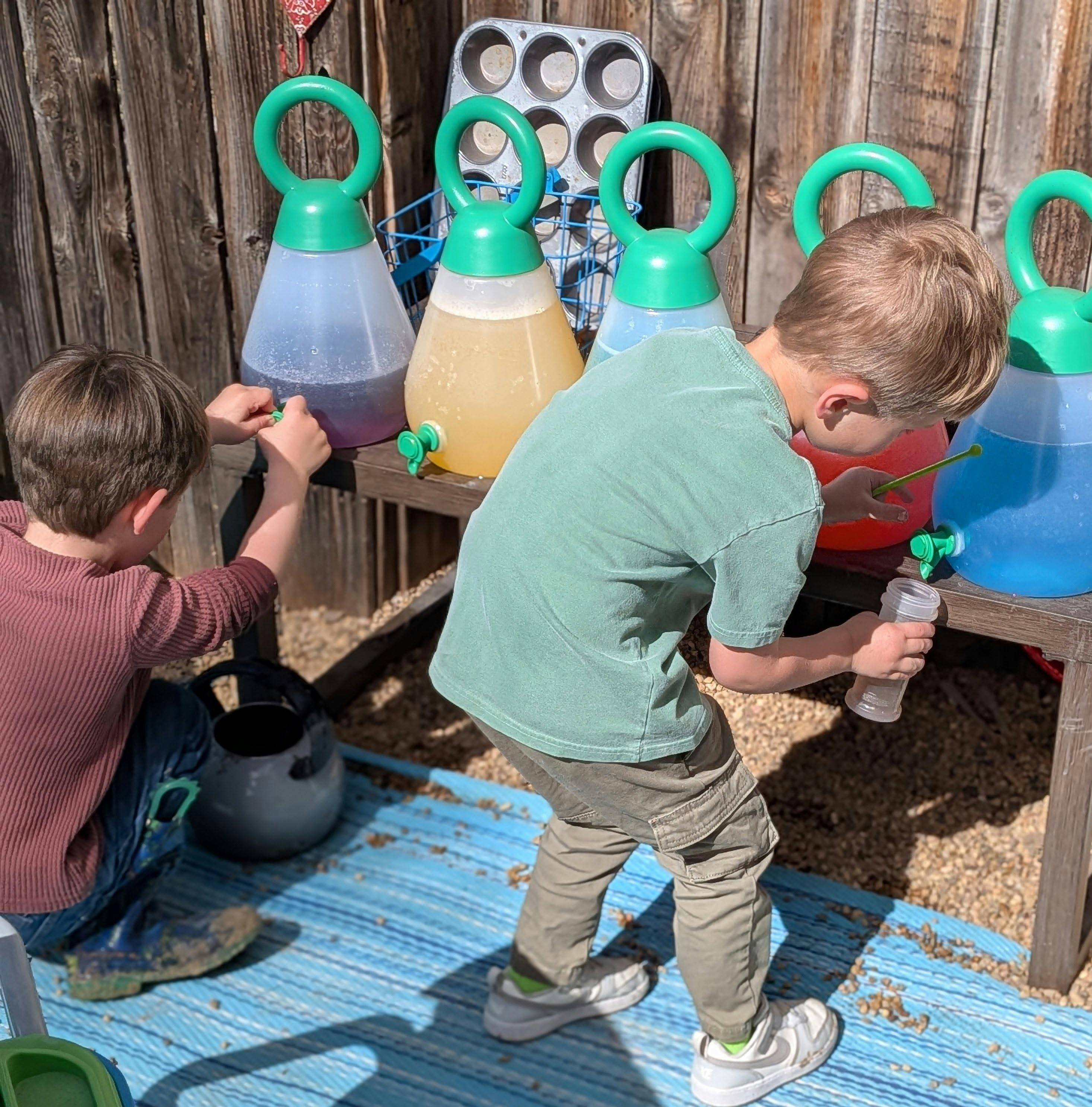 Two children playing with colorful liquid dispensers on a wooden bench