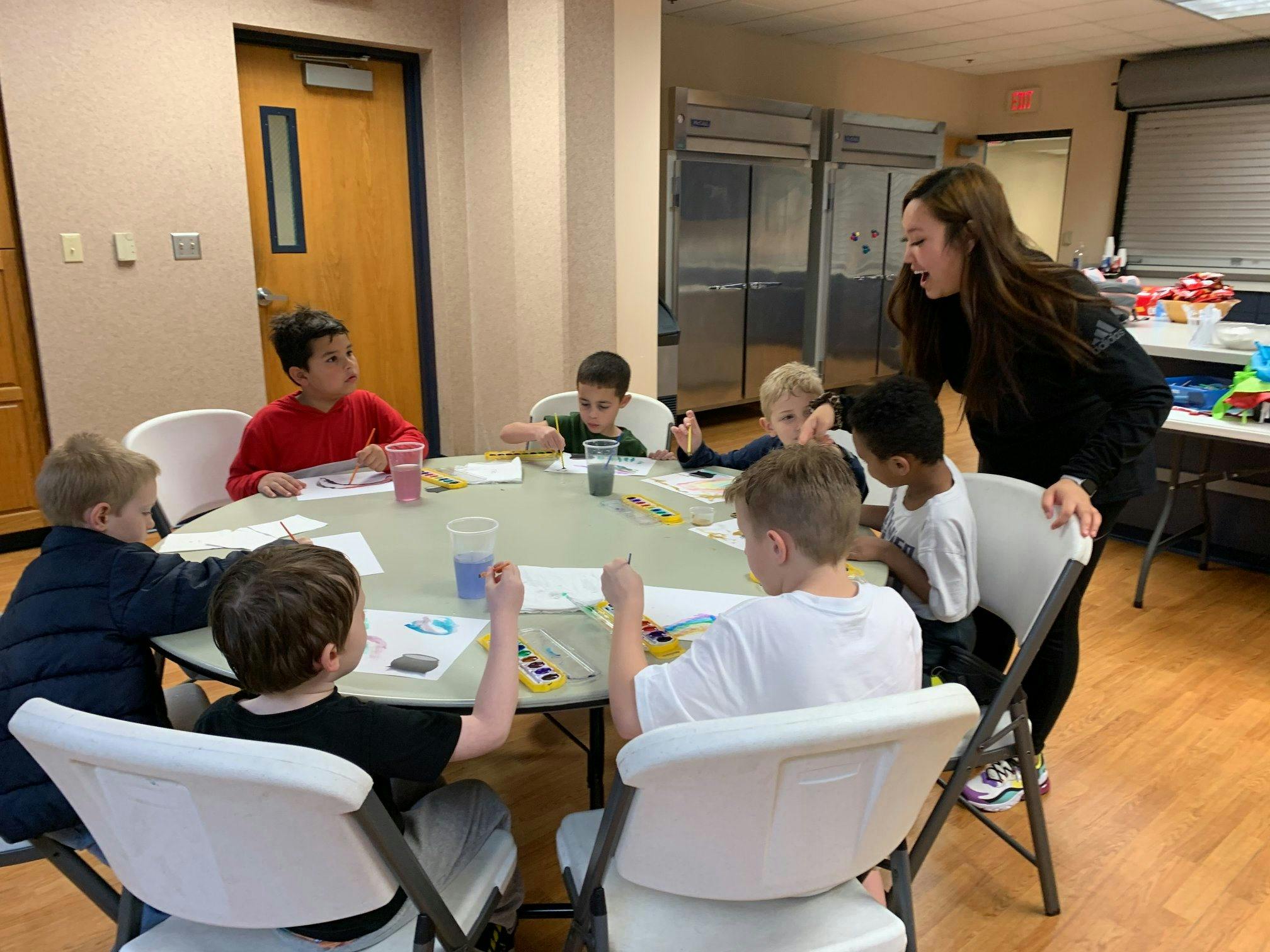 Adult person standing over a table with several children seated around it