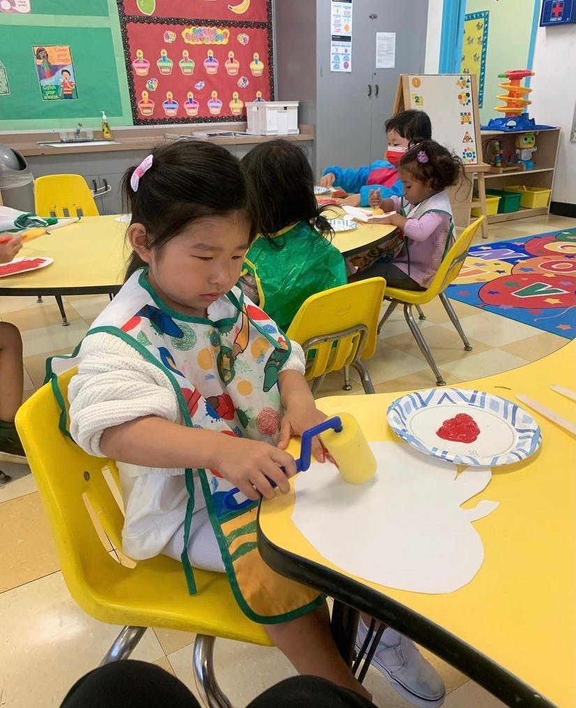 Child painting with a roller at a yellow table in a classroom
