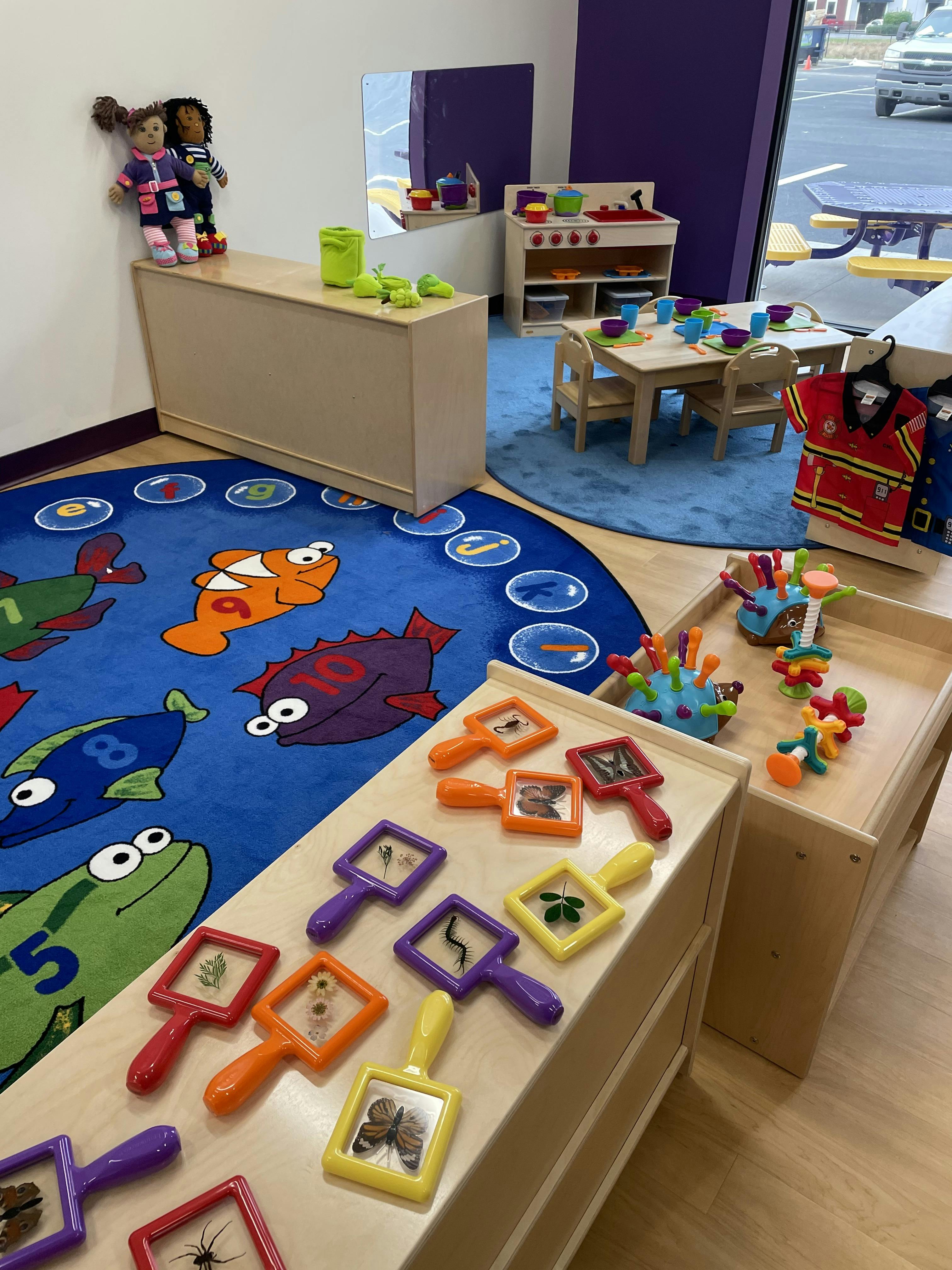 Classroom with play kitchen, small table and chairs, and a colorful rug