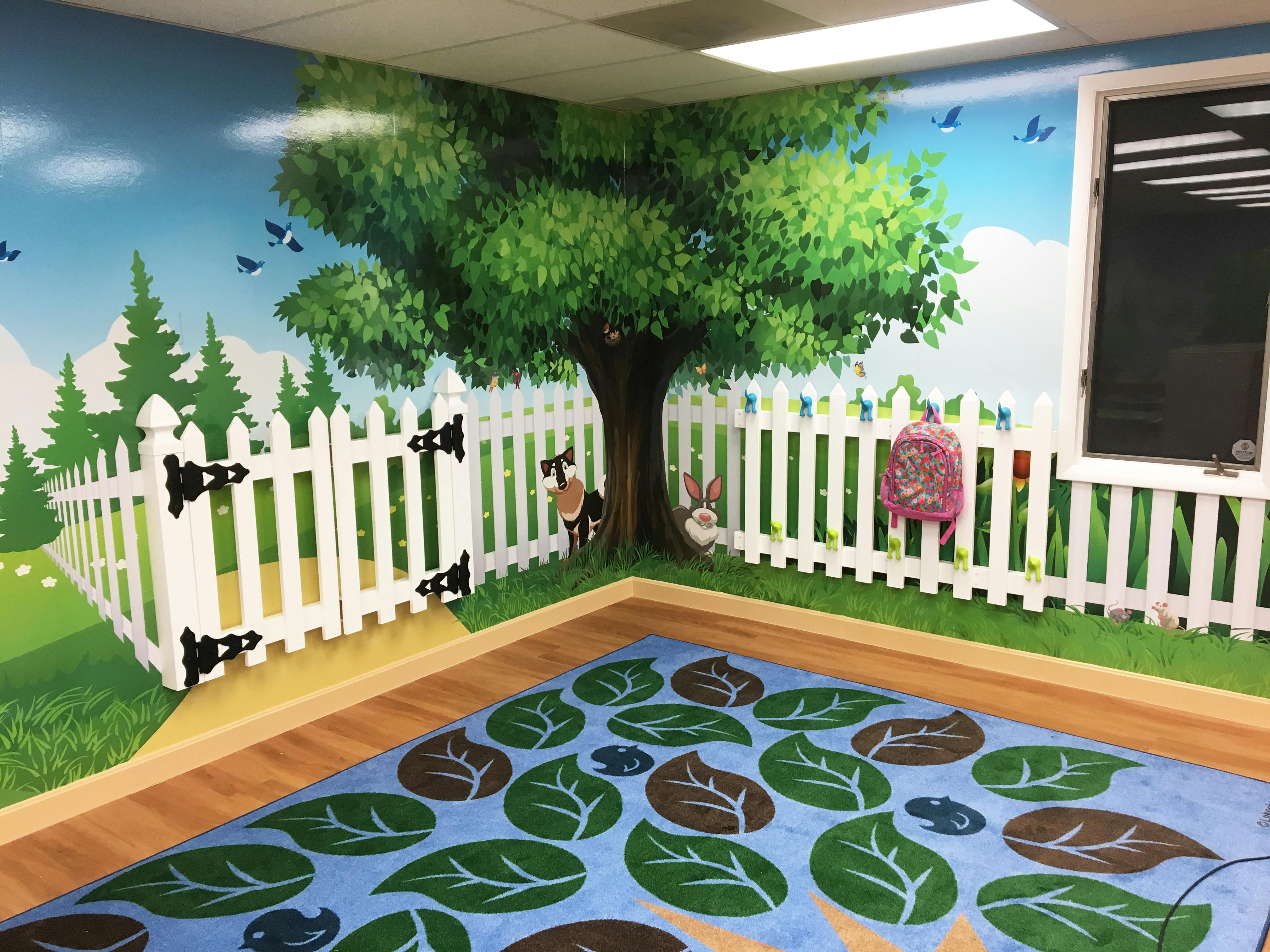 Room with a mural of a tree, fence, and grass, and a rug with leaf patterns