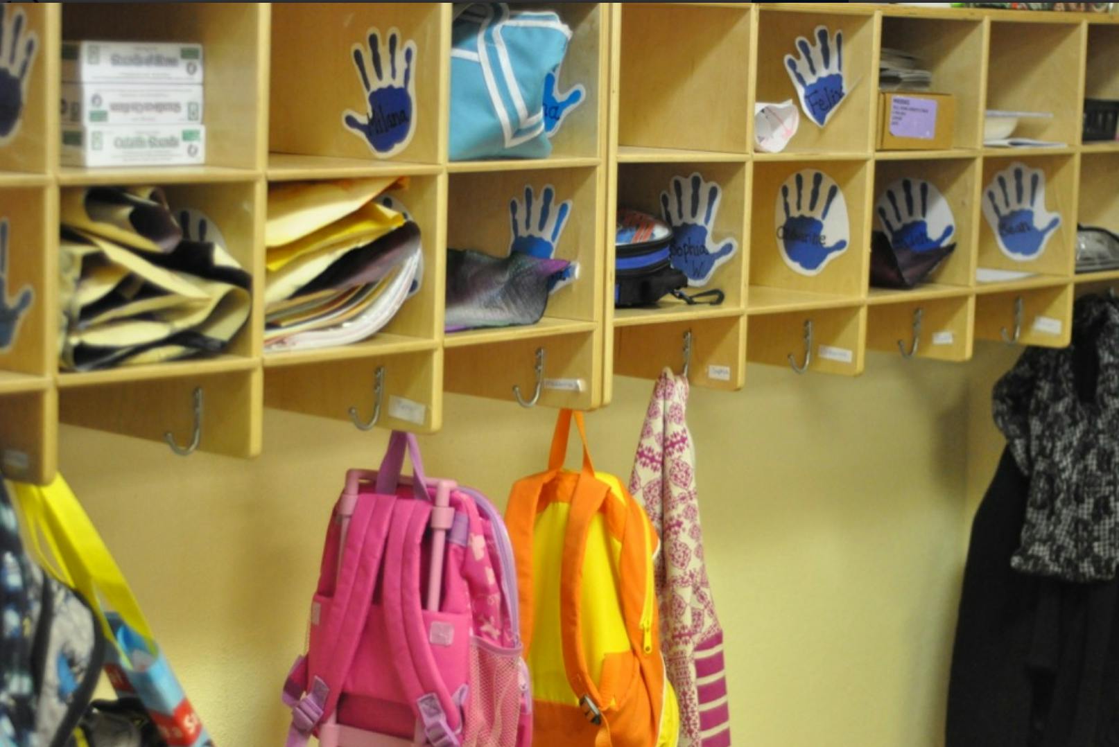 Backpacks hanging below cubbies with papers and handprint cutouts