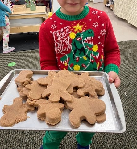 Child in a red sweater holding a tray of gingerbread cookies