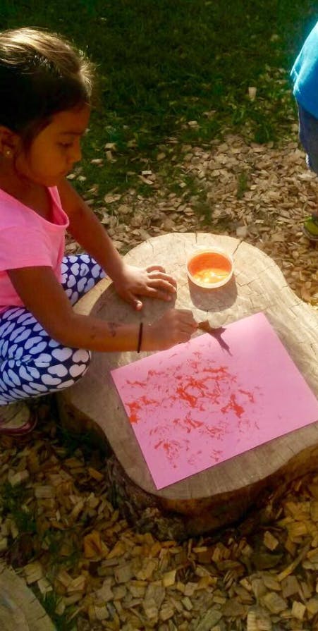 Child painting on pink paper outdoors