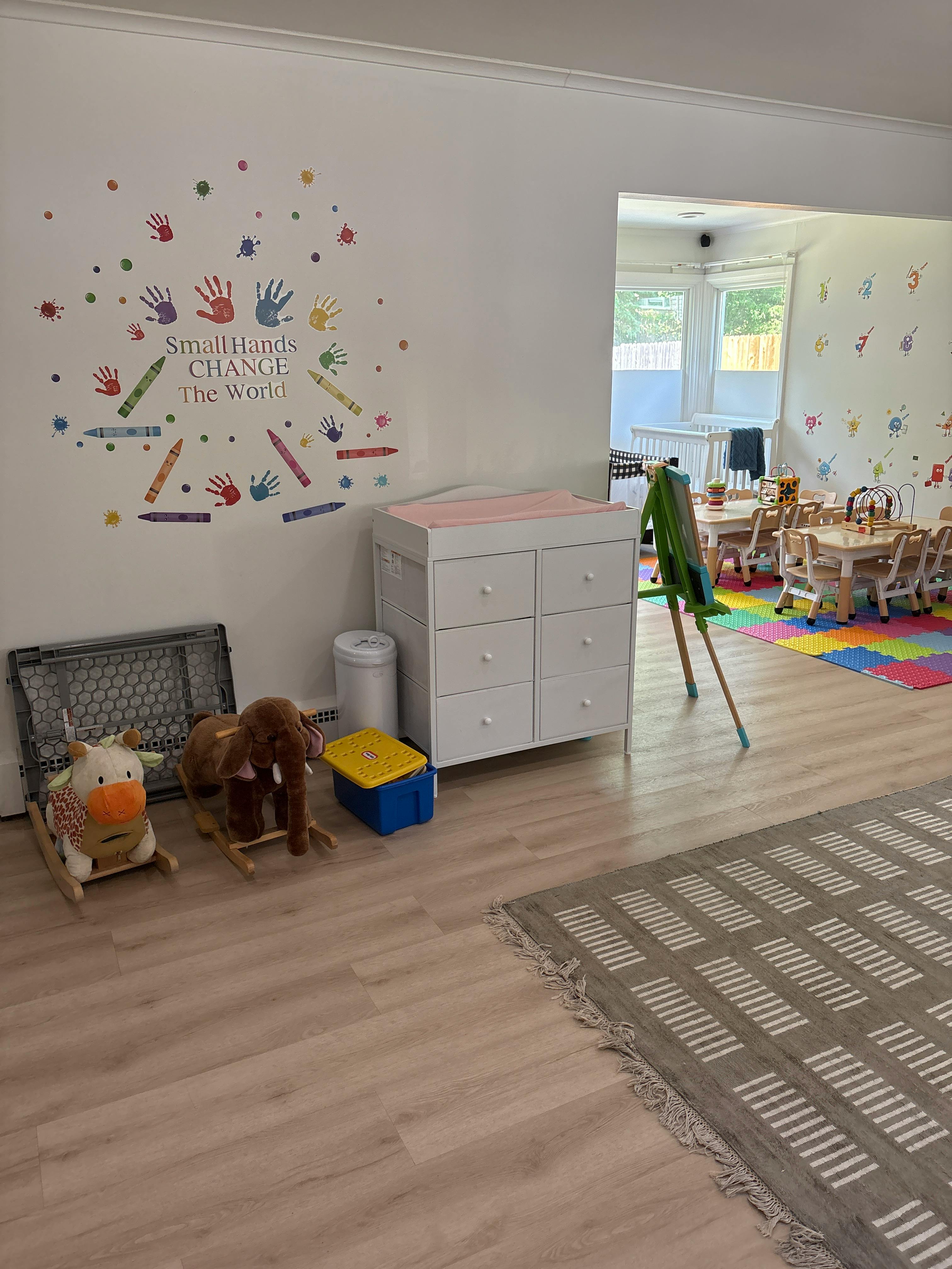 Children's classroom with small tables and chairs, toys, and wall decals