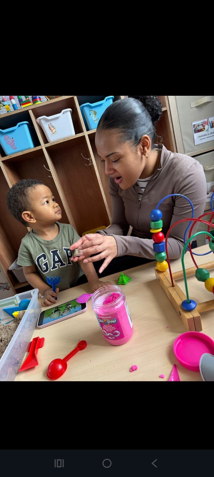 Adult and child playing with sand and toys at a table