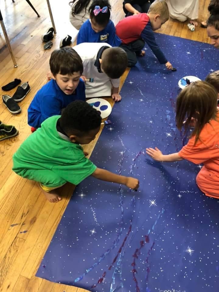 Children painting on a large blue sheet on the floor