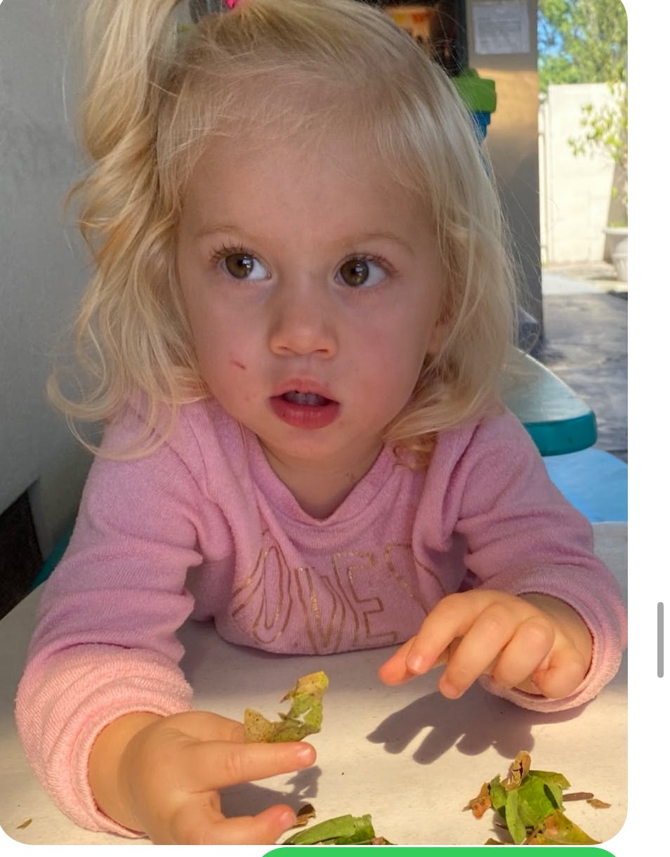 Child with blonde hair holding green food