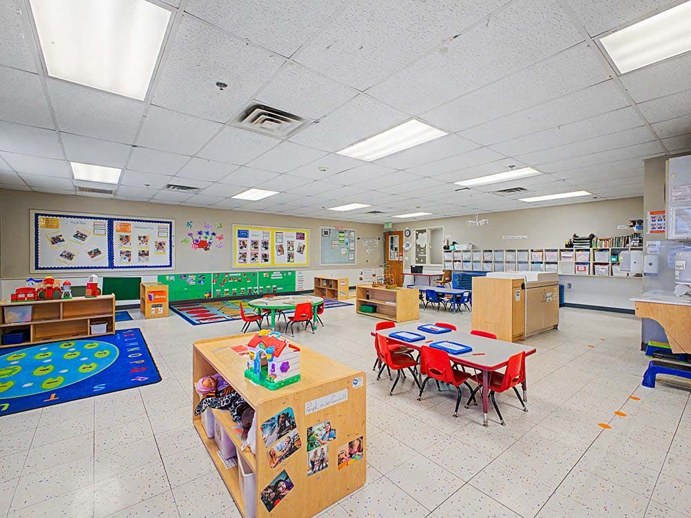 Classroom with small tables and chairs, toys, and bulletin boards